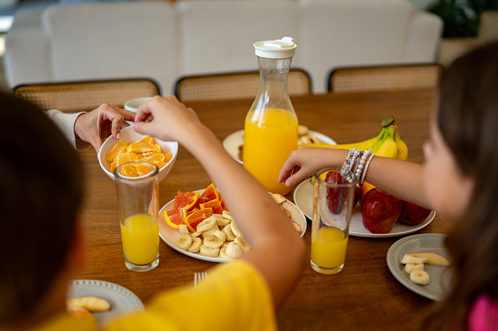 Fotografia de uma mesa de frutas com crianças comendo.
