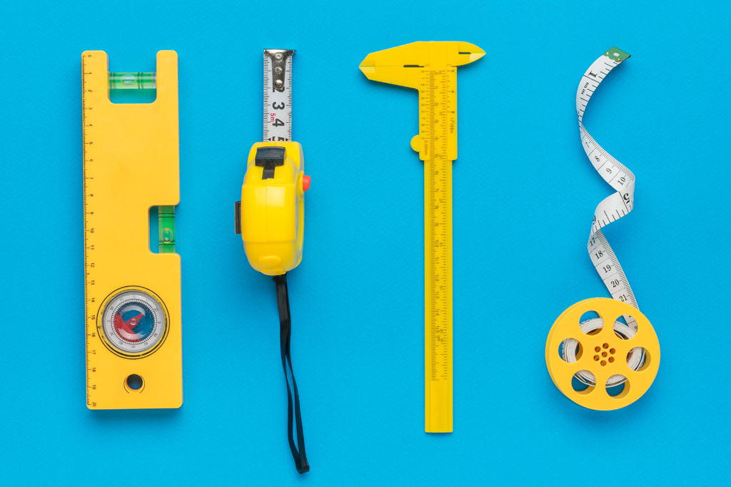 Imagem, em fundo azul, de quatro ferramentas para medição. Vê-se, um nível, uma trena, um paquímetro e uma fita métrica.