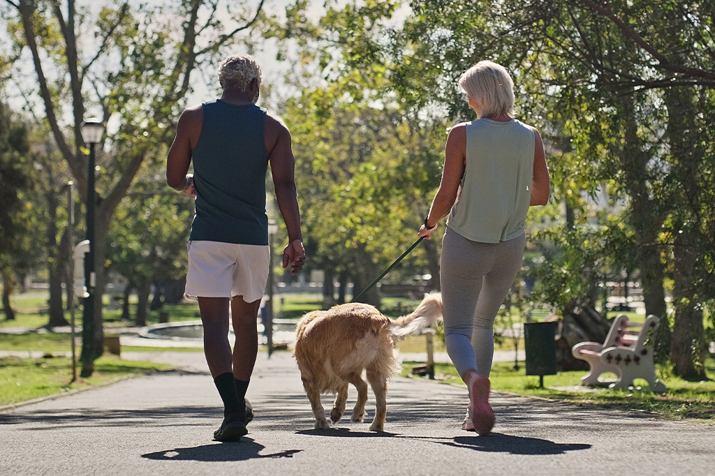 Fotografia de um casal passeando com o seu cachorro no parque.
