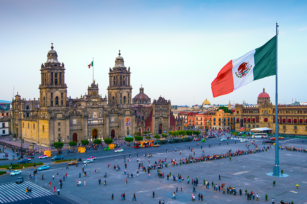 A bandeira mexicana tremula sobre o Zócalo, a praça principal da Cidade do México. A Catedral Metropolitana fica em frente à praça, também conhecida como Praça da Constituição.