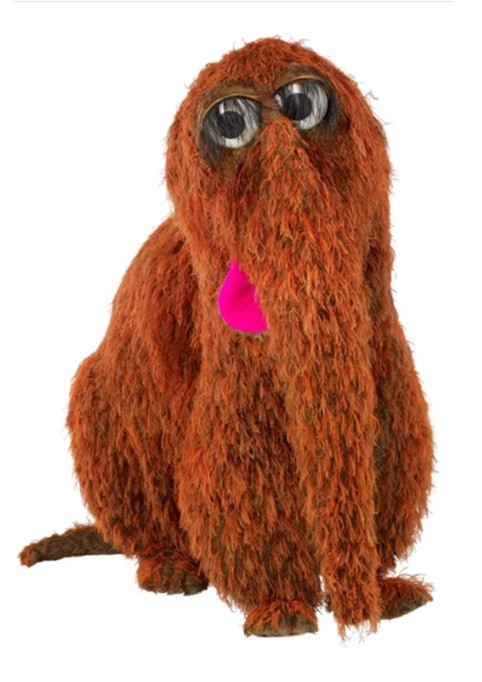 Boneco Snuffy, personagem do programa Vila S&eacute;samo, sentado, com corpo coberto por pelos marrons, olhos grandes e redondos, e uma l&iacute;ngua rosa vibrante saindo da boca, sobre fundo branco