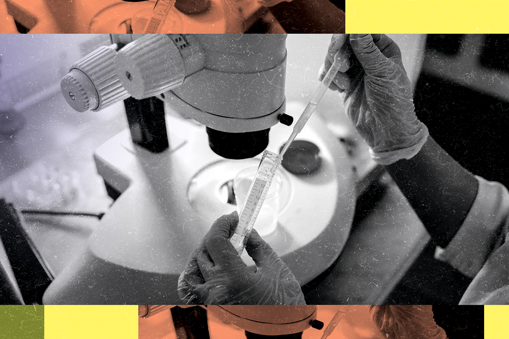 Imagem focada nas mãos de um cientista manipulando uma proveta diante de um microscópio.