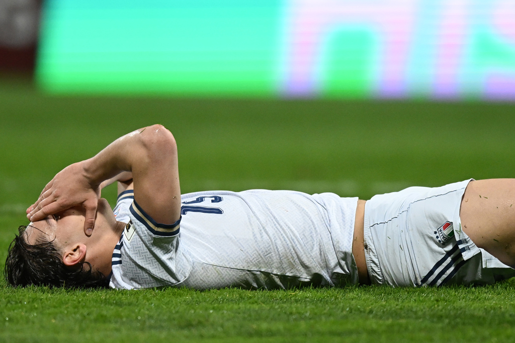 Imagem de um jogador de futebol da seleção italiana deitado no gramado com as mãos no rosto.