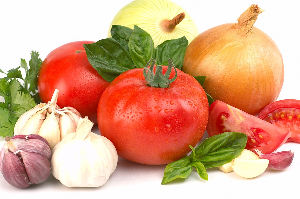 Tomates vermelhos frescos com gotas de água, cebolas amarela e branca, alhos e folhas de manjericão e coentro sobre fundo branco