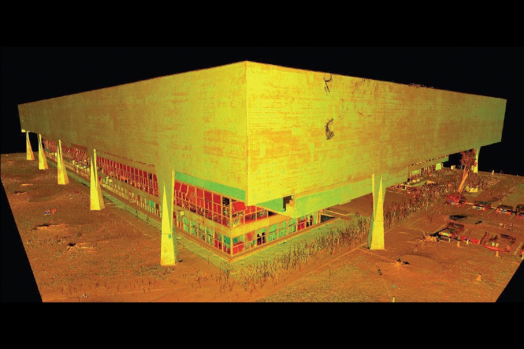 Modelo 3D de um edif&iacute;cio retangular com fachada amarela e janelas vermelhas e azuis, sustentado por pilares triangulares em um terreno marrom-alaranjado, sobre fundo preto