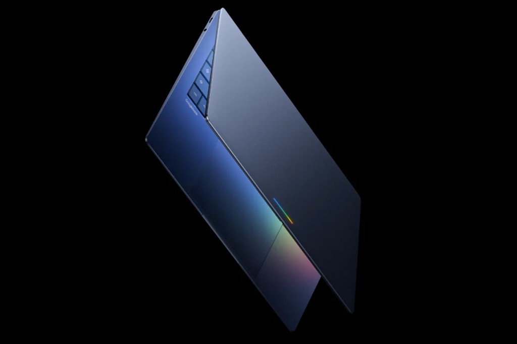 Notebook azul-marinho com teclado e tela parcialmente abertos, exibindo um touchpad com reflexos coloridos e bot&otilde;es de fun&ccedil;&atilde;o na lateral esquerda do teclado, sobre fundo preto.
