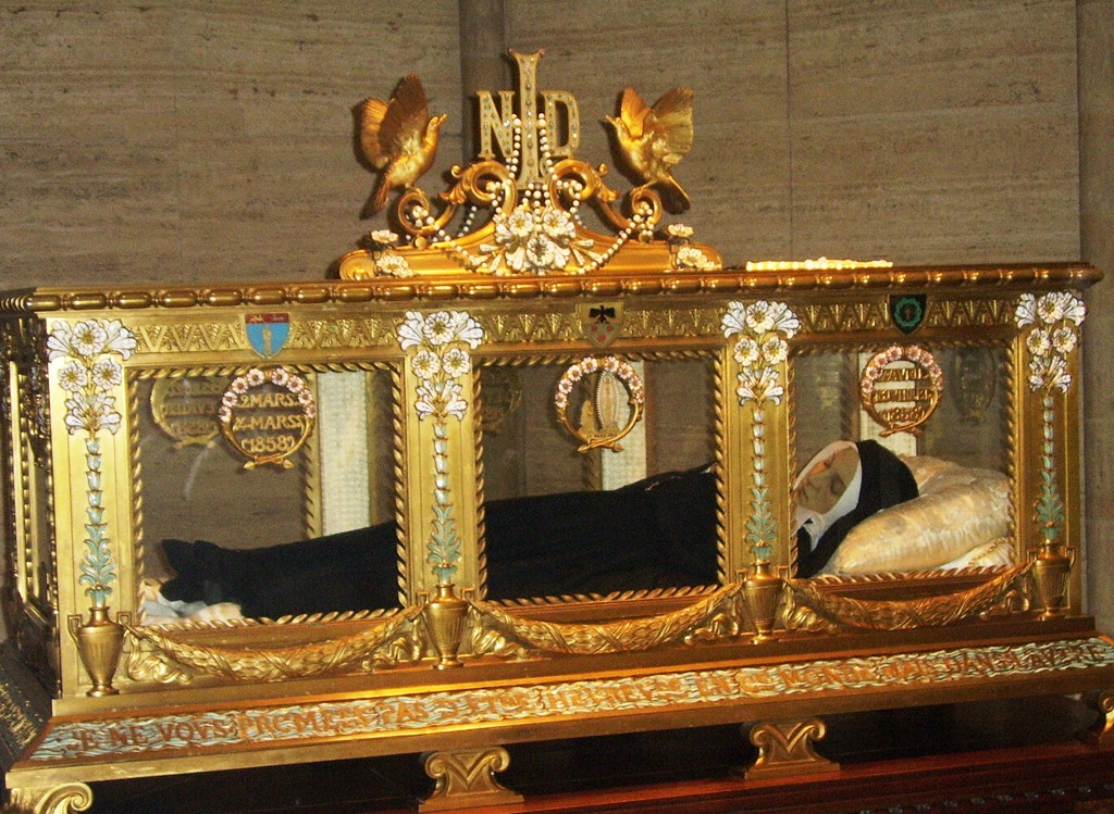 Corpo incorrupto de Santa Bernardete de Lourdes em um relicário dourado e ornamentado, com detalhes em branco e azul, e duas pombas douradas no topo