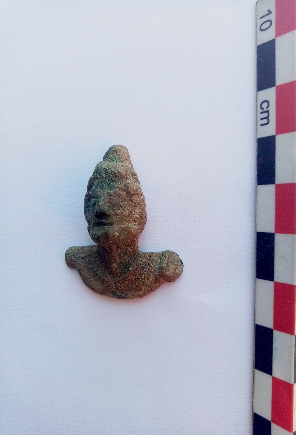 Estatueta antiga de bronze com cabe&ccedil;a e ombros, representando Odisseu, com textura rugosa e colora&ccedil;&atilde;o esverdeada, sobre fundo branco com r&eacute;gua vertical de 10 cm &agrave; direita