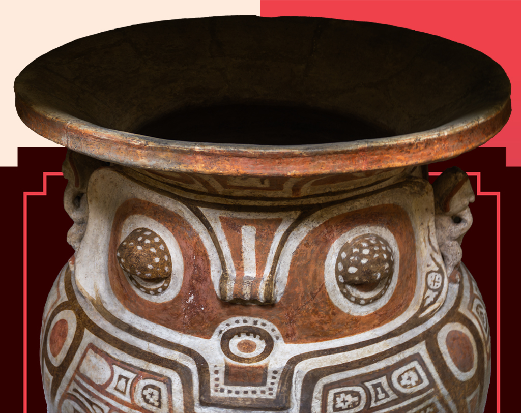 Vaso de cerâmica pré-colombiana com boca larga e borda grossa. O corpo do vaso tem padrões geométricos em tons de marrom, branco e terracota, formando uma face estilizada com olhos grandes e nariz. Há pequenas figuras esculpidas nas laterais, como alças. O fundo é um mosaico de formas geométricas em tons de vermelho e rosa