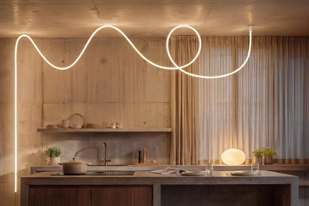 Cozinha moderna com paredes de cimento aparente e iluminação em fita de LED branca que serpenteia pelo teto. Uma panela está no fogão, e pratos e copos sobre a bancada de concreto. Cortinas bege cobrem a janela, e uma luminária oval ilumina a mesa.
